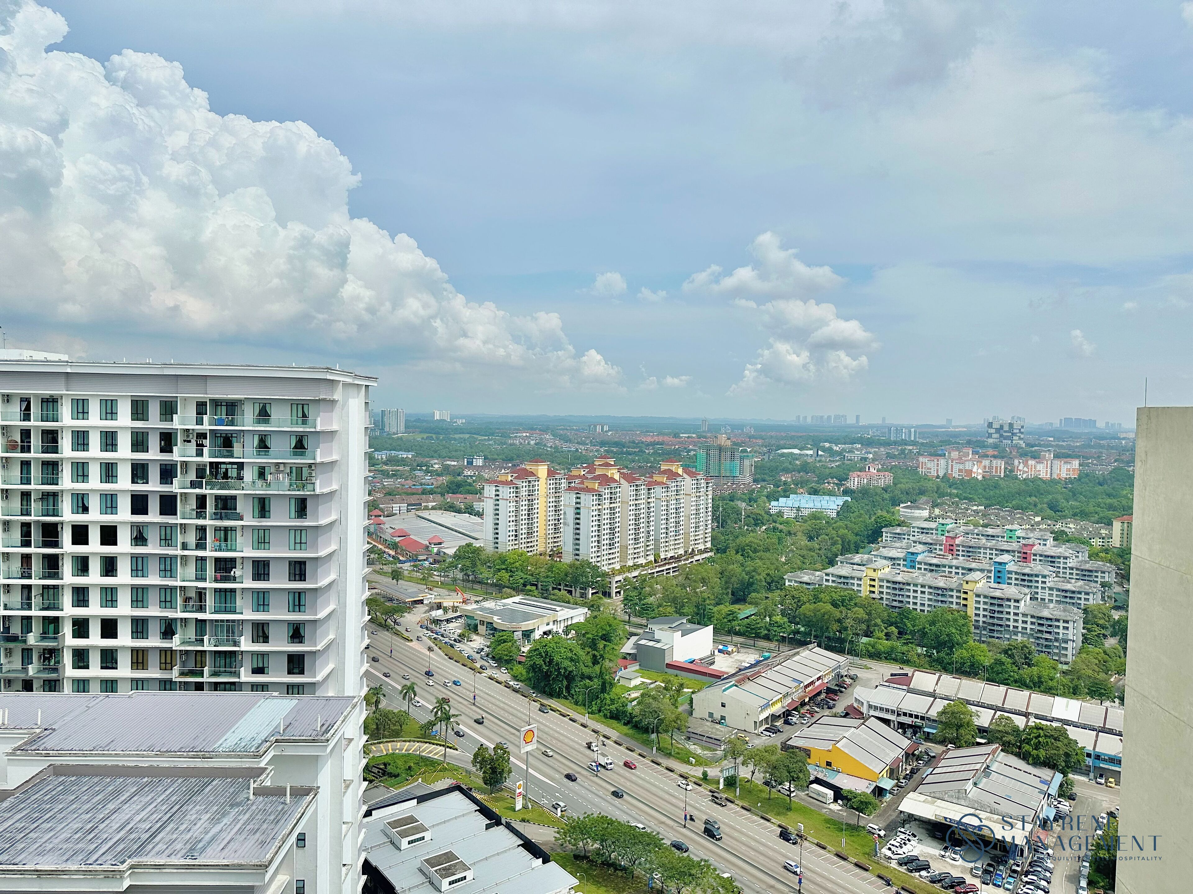 A high-rise building with multiple floors and balconies, surrounded by a cityscape with various buildings and a busy road.