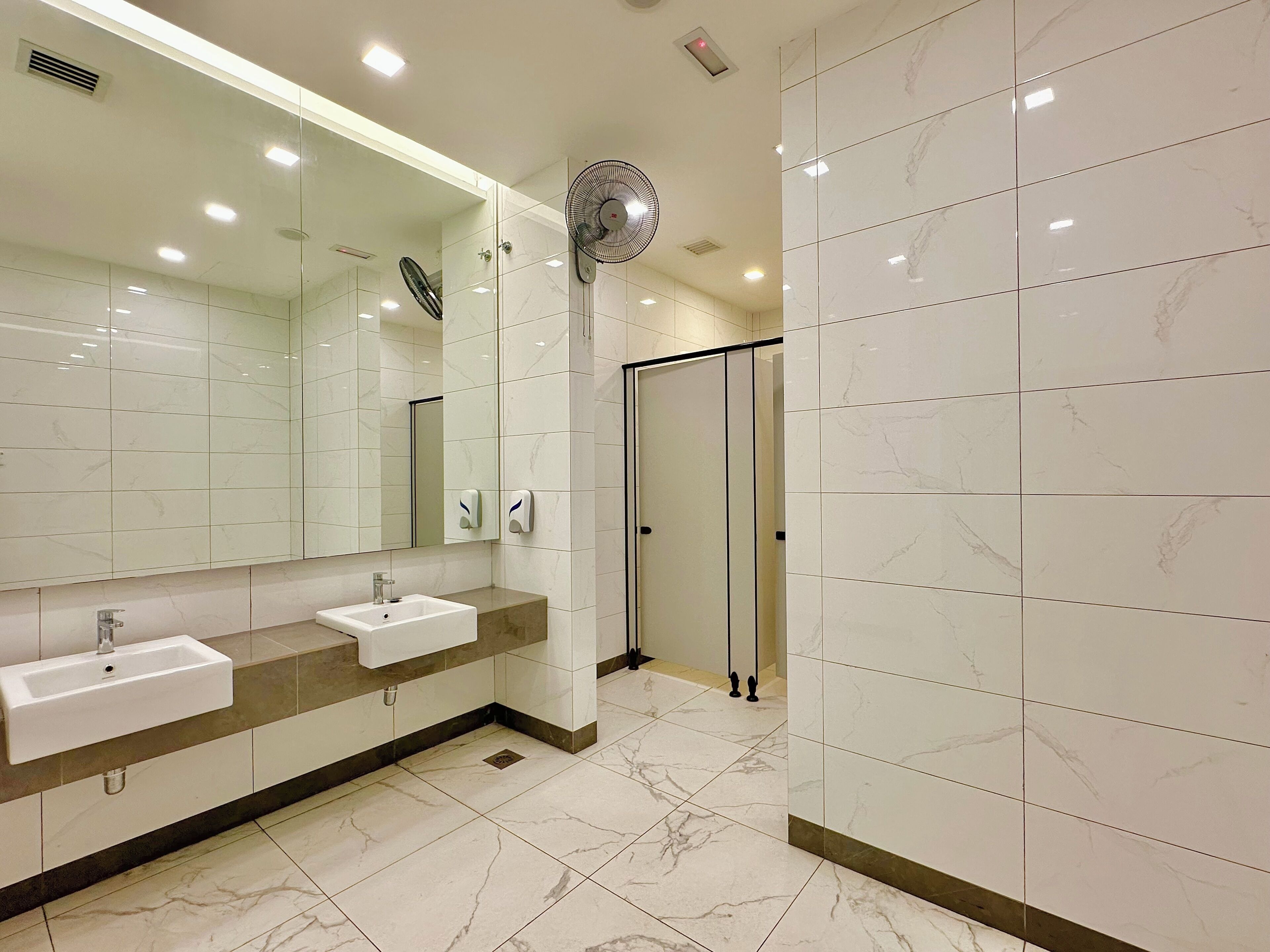 A modern bathroom with two sinks, a large mirror, a fan, and a glass shower enclosure.