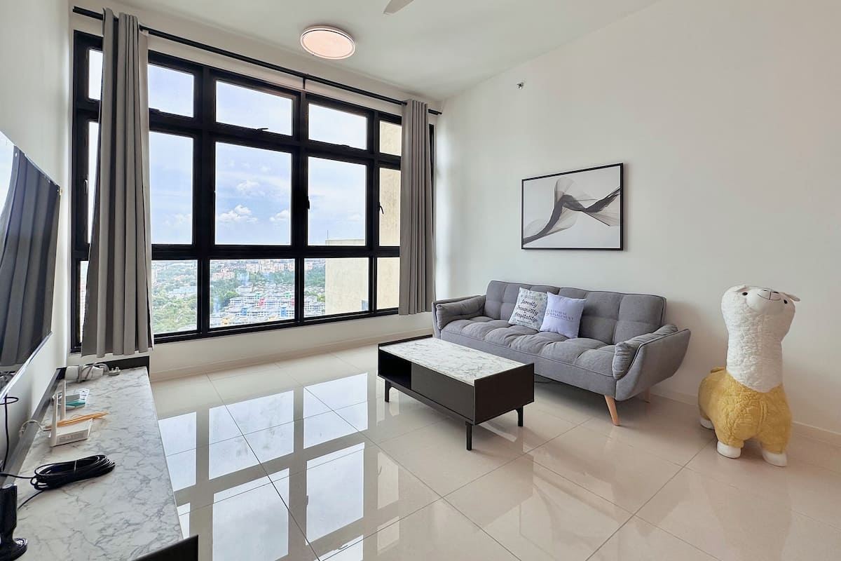 A modern living room with a large window, a grey sofa, a marble coffee table, and a ceiling fan.