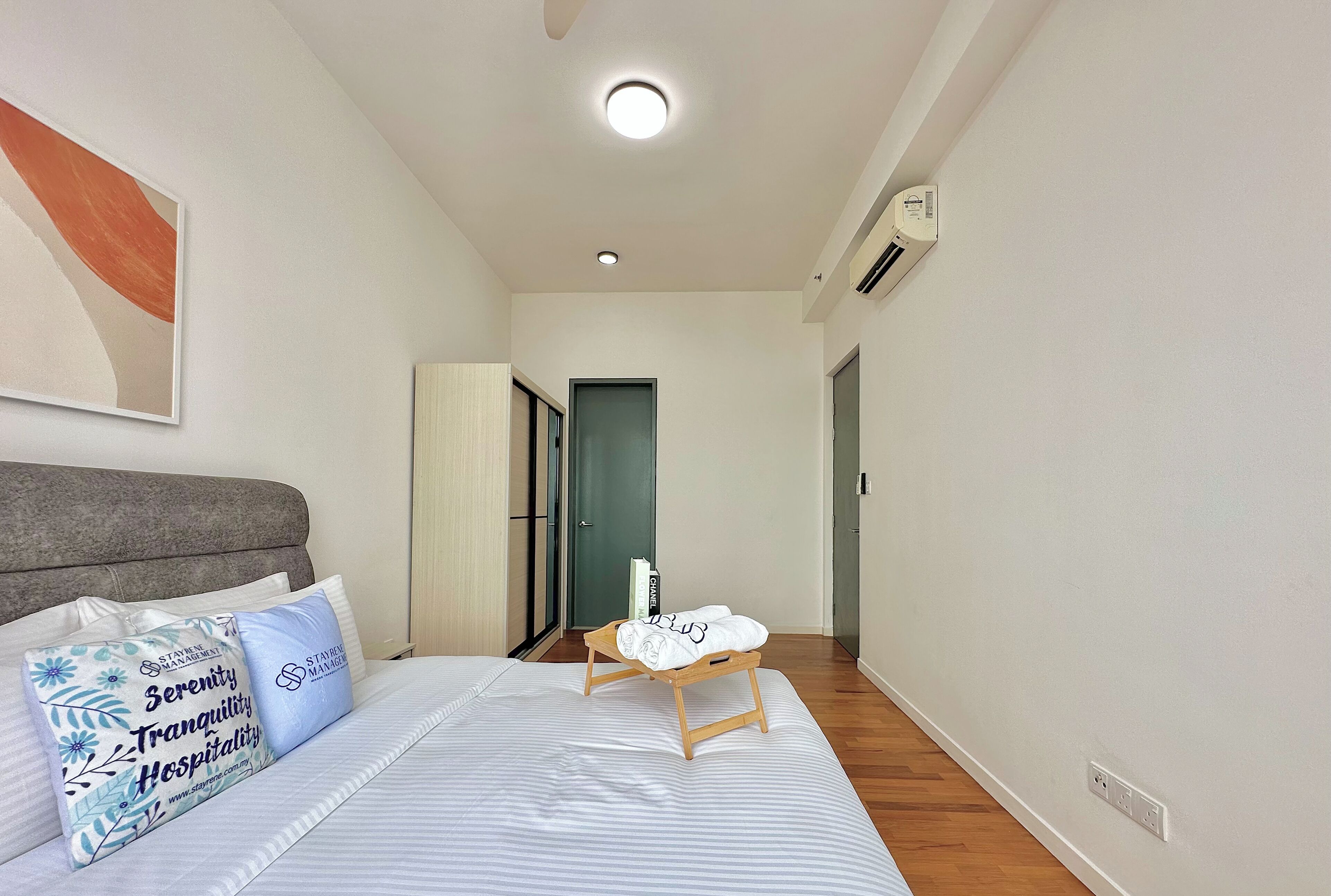 A hotel room with a bed, pillows, a bedside table, a door, and a wall-mounted air conditioner.