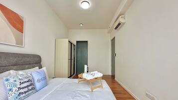 A hotel room with a bed, pillows, a bedside table, a door, and a wall-mounted air conditioner.