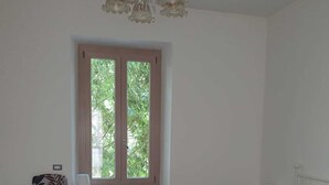 A bedroom with two beds, a window, a chair, and a radiator. - Illy House in downtown Alghero. (Alghero)