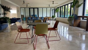 A spacious room with a large table and chairs, large windows, ceiling fans, and potted plants.