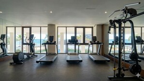A gym with treadmills, elliptical machines, and weight equipment, large windows with a view of the ocean.