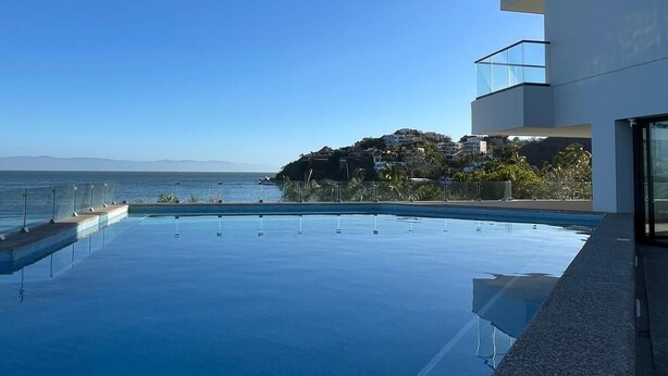 A modern building with a large infinity pool overlooking the ocean.