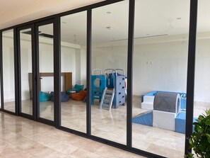 A room with a sliding glass door, a play area with a slide and climbing structure, and a sofa. - Wake up to the Sound of the Sea (Cruz de Huanacaxtle)