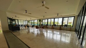 A spacious indoor area with multiple ceiling fans, large windows, and a tiled floor.