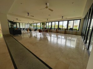 Um espaço amplo e interno, com várias ventoinhas no teto, grandes janelas e piso em azulejos.