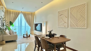 A modern living room with a dining area, large windows, a flat-screen TV, and decorative wall art. - Paragon Suites CIQ By Stayrene (Johor Bahru)