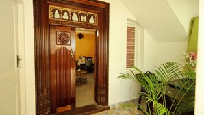 Uma porta de madeira com esculturas detalhadas, chão de azulejos e um vaso de planta ao lado da entrada.