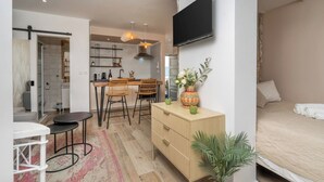 Een kleine hotelkamer met een bed, een bureau, een stoel, een aan de muur bevestigde televisie en een kitchenette.