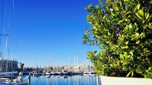 A marina with boats docked, a clear blue sky, and a well-maintained hedge.