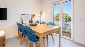 Un comedor con una mesa de madera, sillas azules, un jarrón con plantas secas y un cuadro en la pared.
