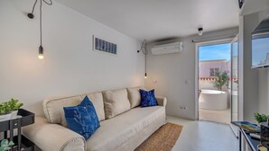 A modern living room with a sofa, a small table, a wall-mounted air conditioner, and a view of the outside. - Cozy 1-bedroom house in the historic old town of Portimão. (Portimão)