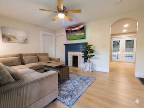 A living room with a sofa, a coffee table, a fireplace, a television, and a ceiling fan.