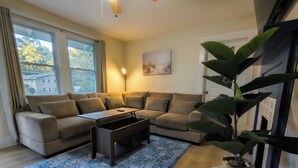 Un salon avec un canapé d’angle, une table basse, un tapis à motifs bleus et une plante en pot.