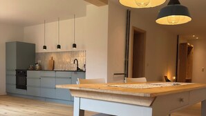 Une cuisine moderne avec des meubles de couleur bleu clair, une table à manger en bois et des luminaires suspendus.
