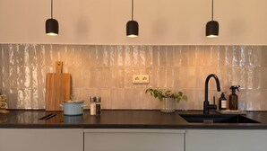 Une cuisine moderne avec trois luminaires suspendus, une planche à découper en bois, un pot bleu et un évier avec un robinet.