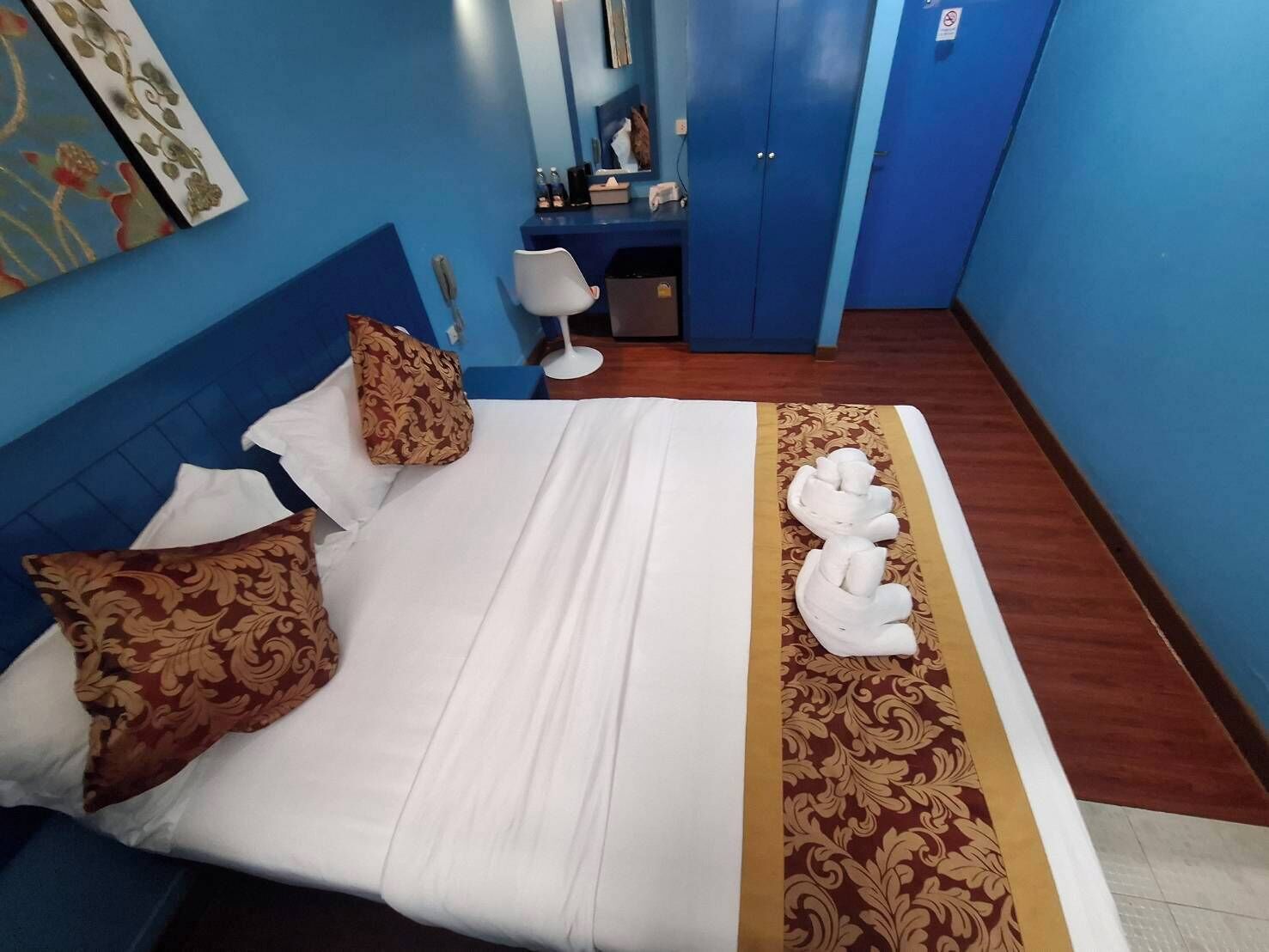 A hotel room with a bed, pillows, a desk, a mirror, and a blue wall.