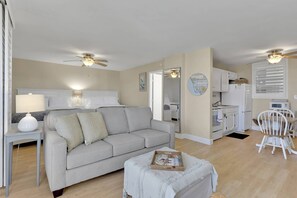 Ein kompakter Wohnbereich mit Sofa, einem kleinen Tisch, Deckenventilator und einer Küchenzeile.