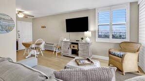 A living room with a television, a dining area with chairs, a sofa, and a window with blinds.