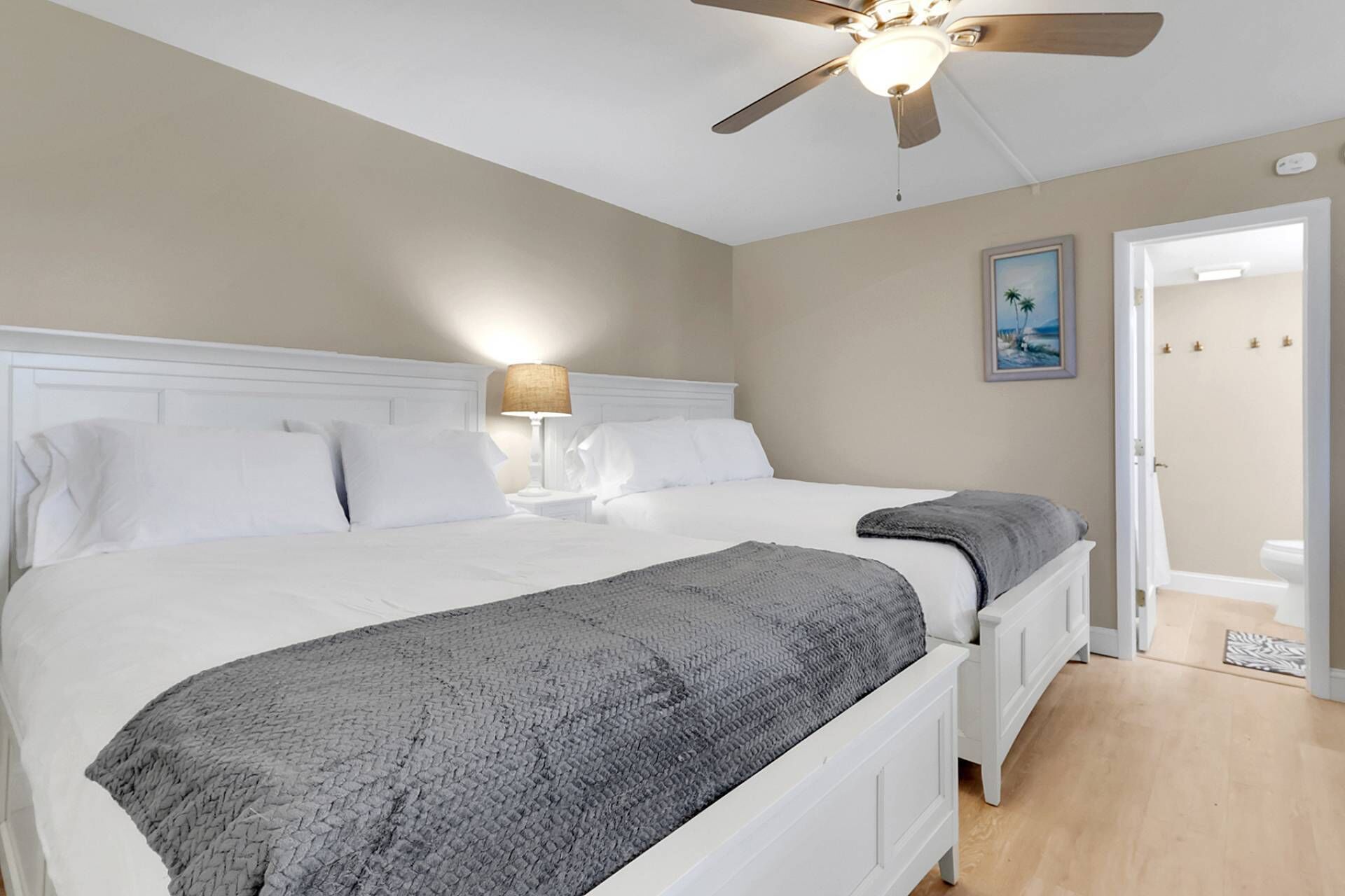 A bedroom with a large bed, a ceiling fan, a bedside lamp, and a door leading to another room.