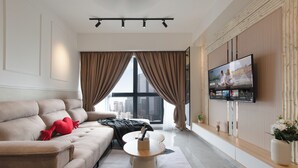 Una sala de estar moderna con un sofá, una mesa de centro, un televisor de pantalla plana montado en la pared y un amplio ventanal con cortinas.