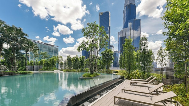 Una piscina en la azotea con sillones de descanso, rodeada de follaje y edificios modernos.