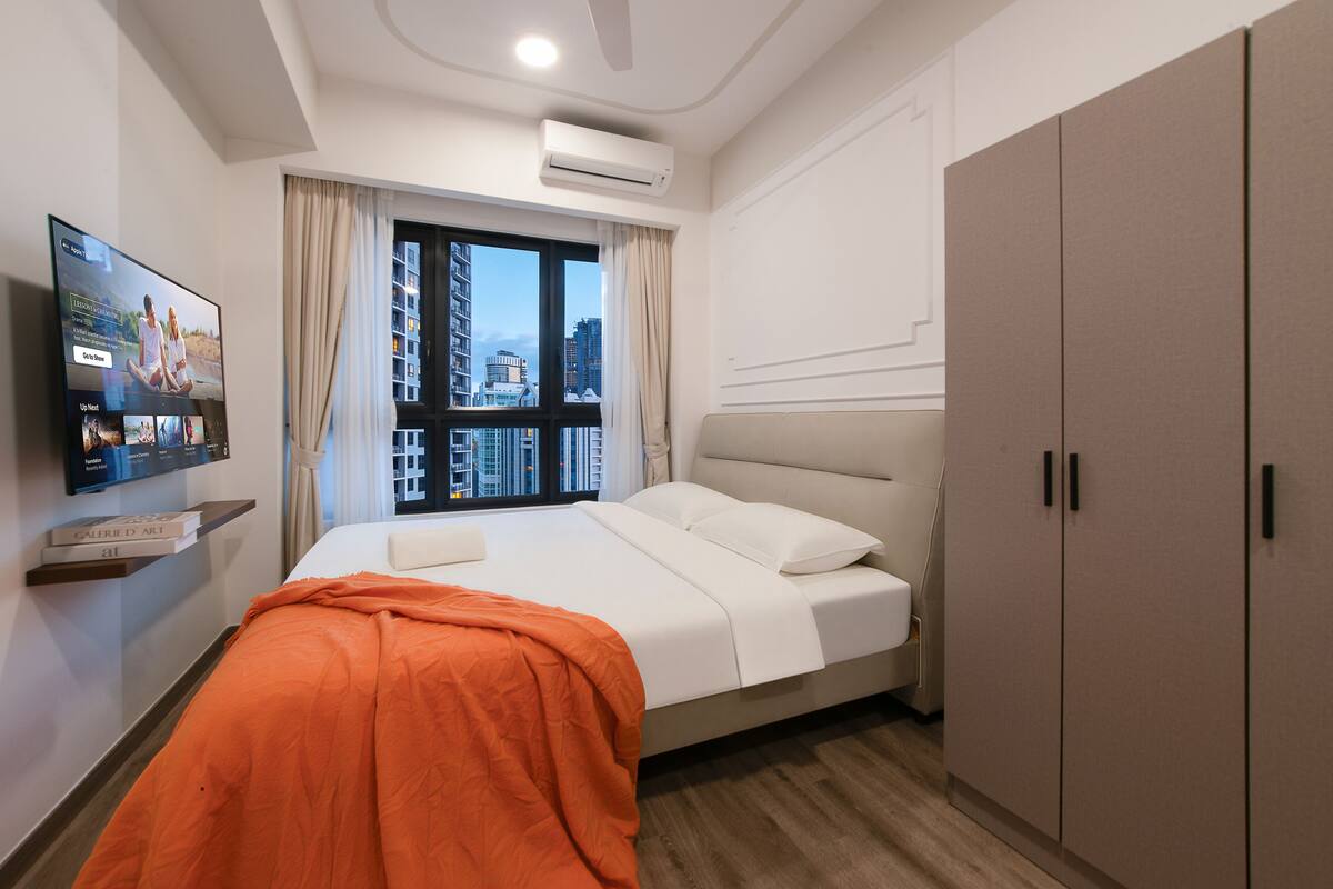 Habitació d'hotel moderna amb un llit, un televisor penjat a la paret, una finestra amb cortines i un armari.