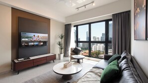 Una sala de estar moderna con una televisión de pantalla plana, un sofá, una mesa de centro y un amplio ventanal con vistas a la ciudad.