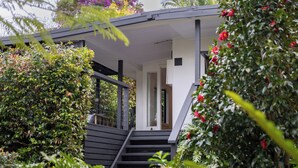 Une maison moderne dotée d’un porche abrité, d’un escalier menant à l’entrée et d’une végétation luxuriante qui entoure la propriété.
