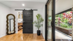 Un intérieur moderne avec un plancher en bois, une porte coulissante noire, une plante en pot et une vue sur un jardin, visible à travers une porte vitrée.