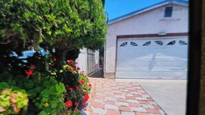 Una strada asfaltata conduce a un garage, fiancheggiata da un siepe con fiori rossi e un edificio con una porta garage bianca.