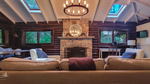A log cabin interior with a stone fireplace, leather sofas, a dining table, and a TV. - Escape to The Hideout, a charming 2-bedroom cabin in Boothbay Harbor. (Boothbay Harbor)