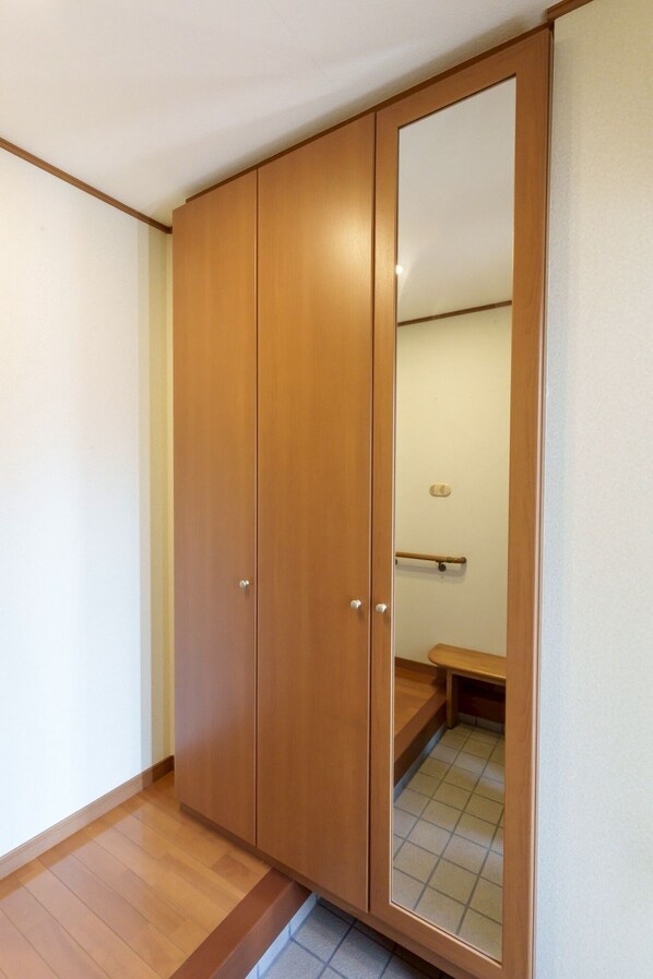 A wooden wardrobe with a mirror, a small bench, and a tiled floor.