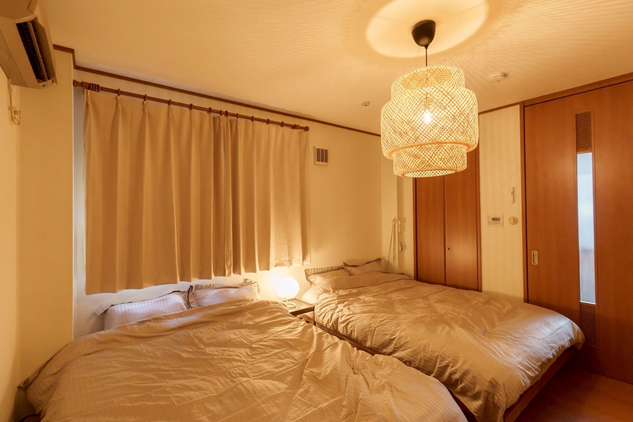 Una habitación con dos camas, ventilador de techo y lámpara de fibra.