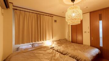 Una habitación con dos camas, ventilador de techo y lámpara de fibra.