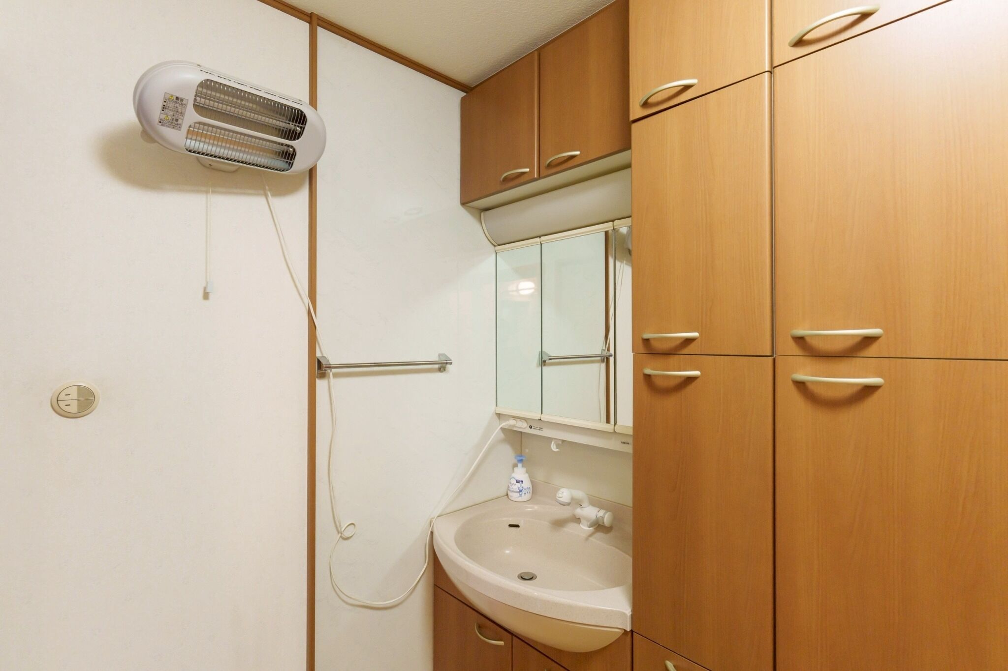 A compact bathroom with a wall-mounted heater, a sink with a mirror, and wooden cabinets.