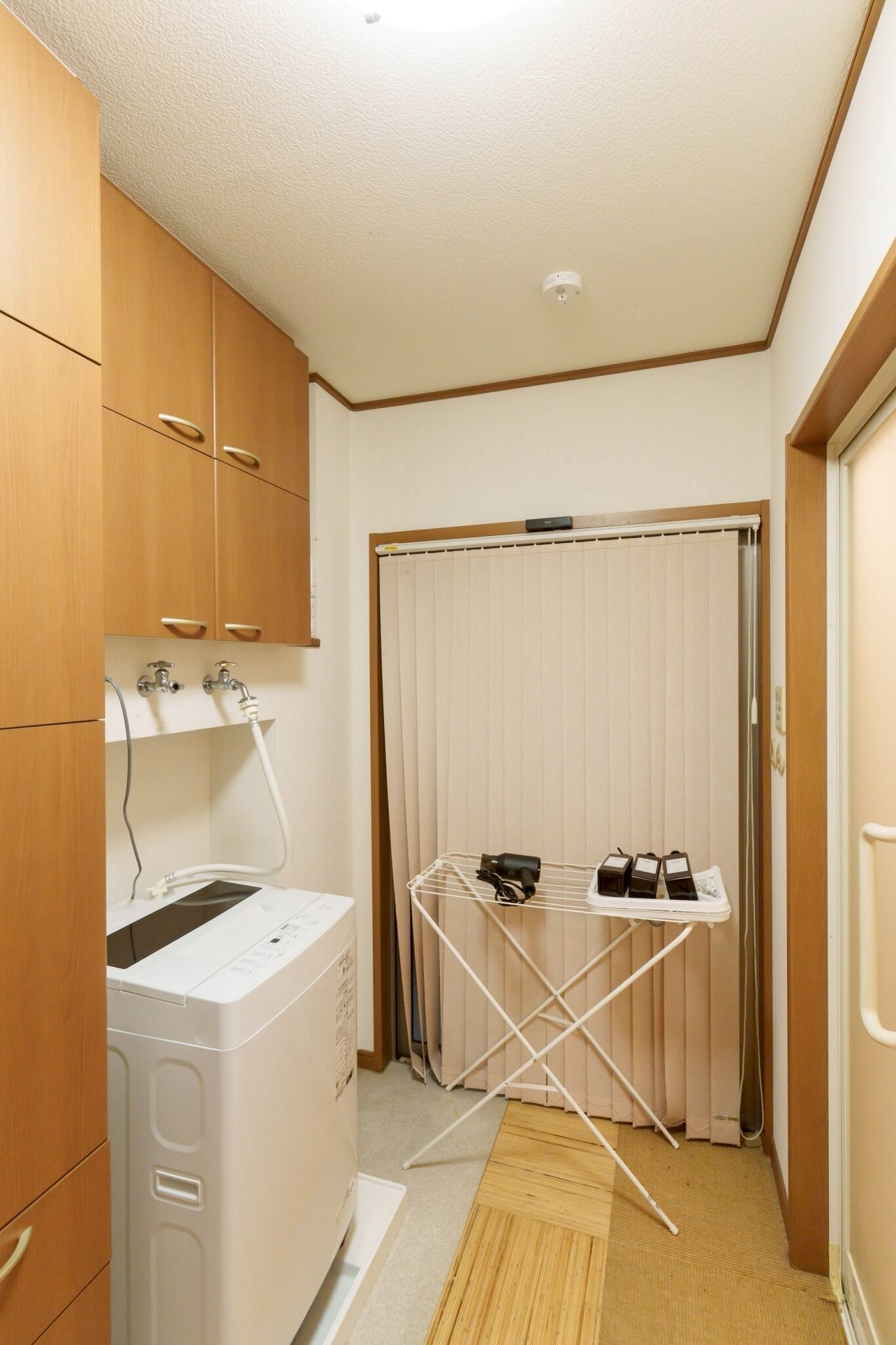 A laundry area with a washing machine, drying rack, and wooden cabinets.