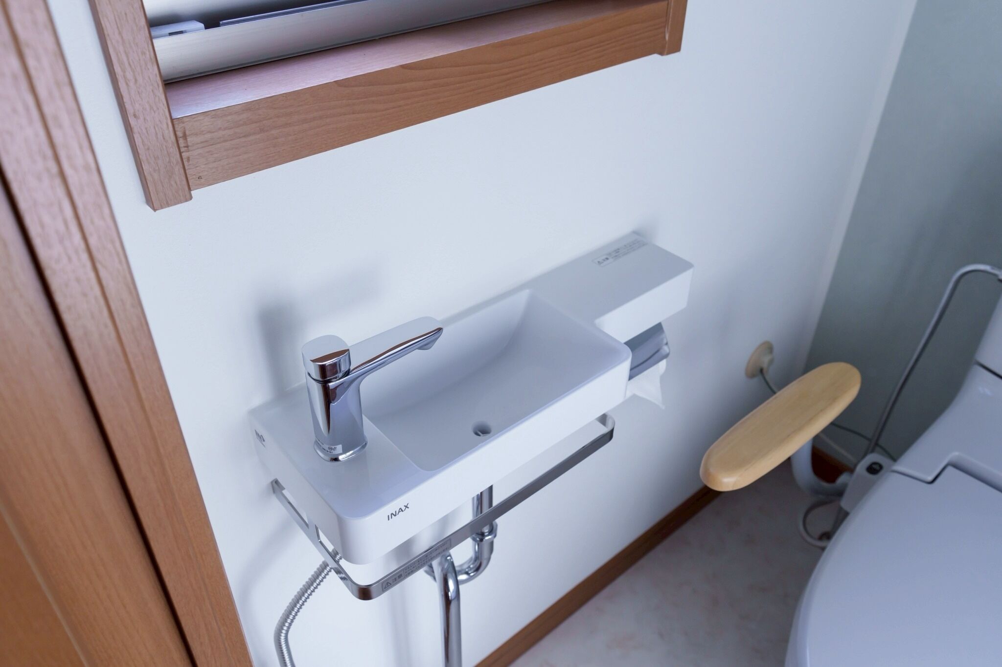A modern bathroom with a white sink, chrome faucet, and a wooden toilet seat.