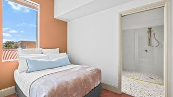 A bedroom with a bed, a window, and a shower area.