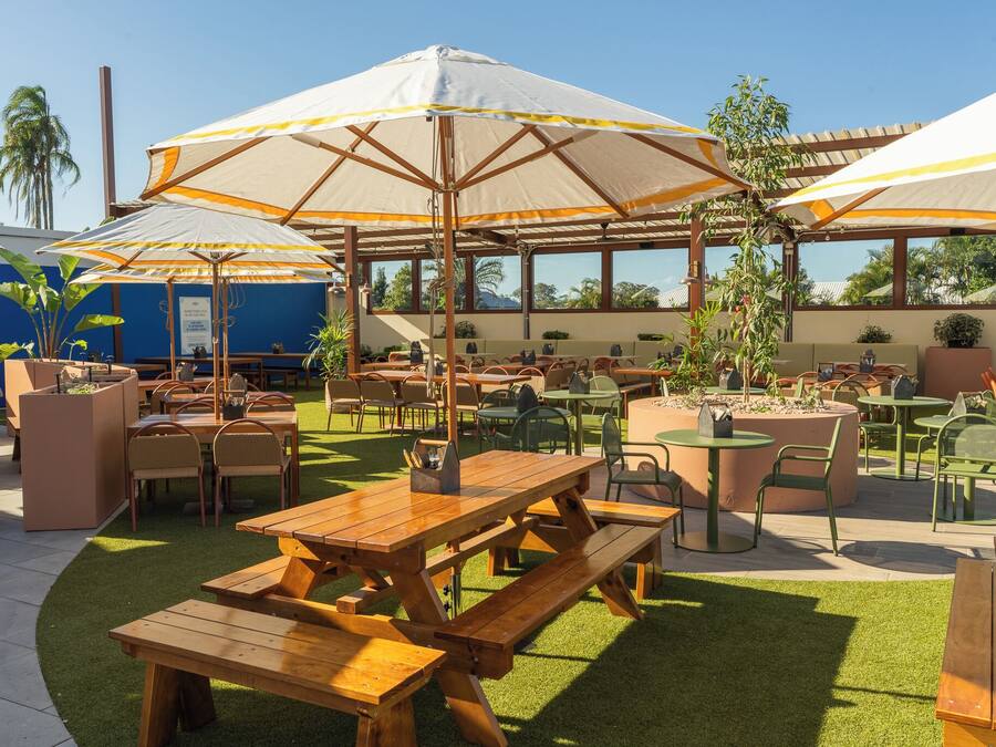 Een terras buiten met houten tafels en stoelen, parasols en potplanten.
