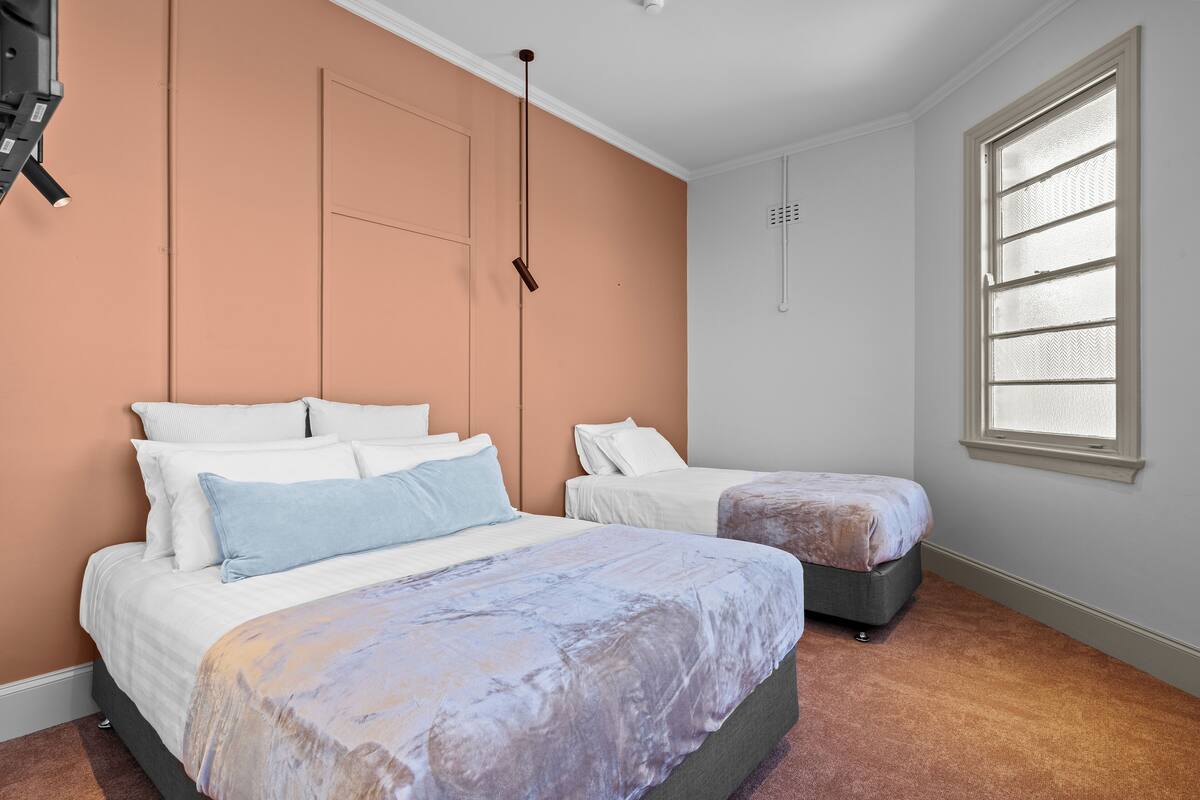 A bedroom with two beds, a large window with blinds, and a ceiling light fixture.