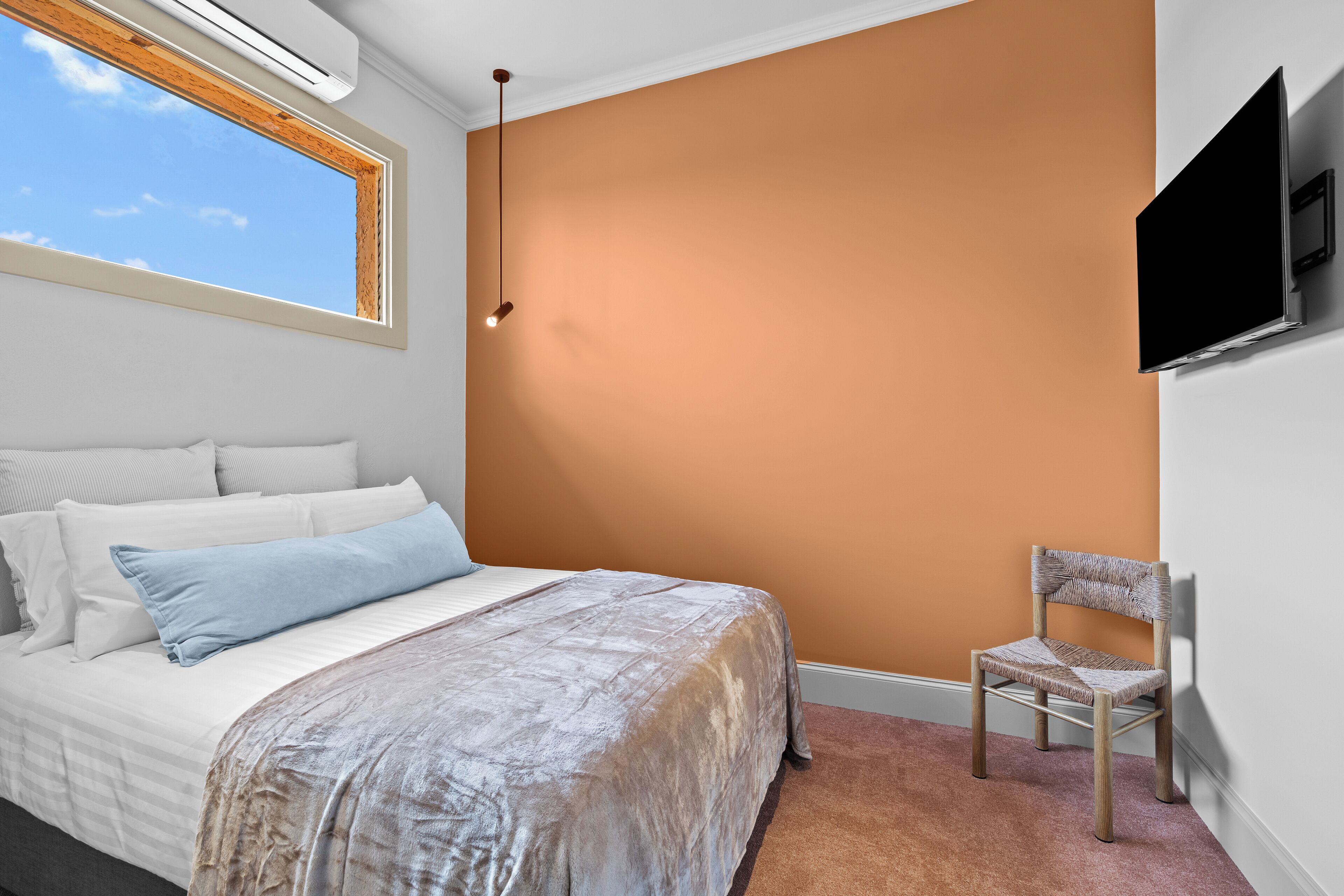 A bedroom with a bed, a chair, a TV, and a window.