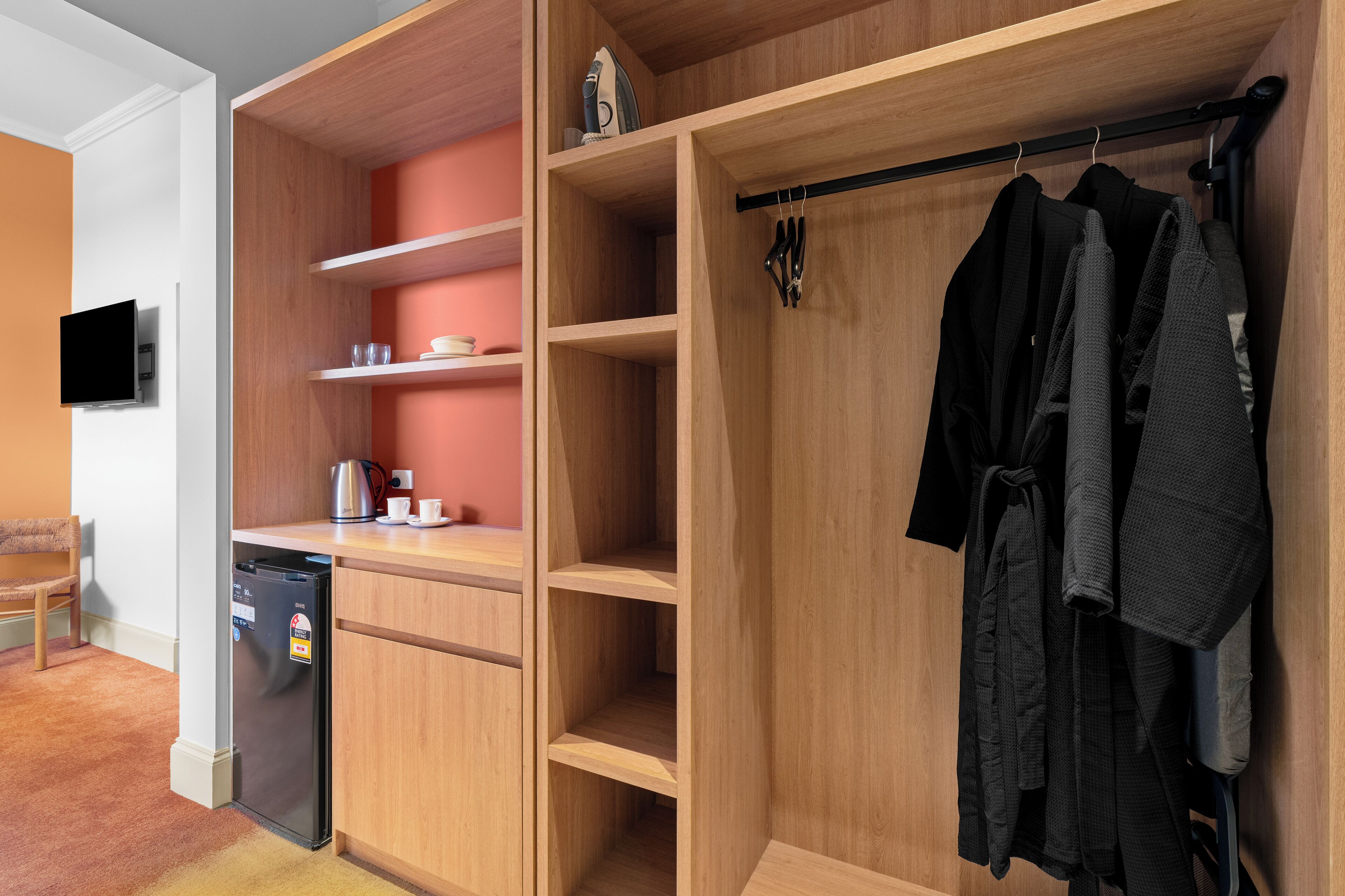 A compact room with a built-in wardrobe, a small kitchenette, and a seating area.