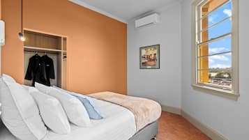 A bedroom with a bed, a closet, an air conditioning unit, a window with a view, and a framed picture on the wall.
