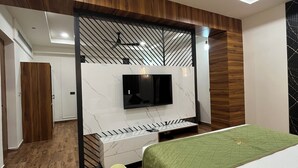 Un dormitorio moderno con televisor montado en una pared de mármol, ventilador de techo y cama con cubrecama verde.