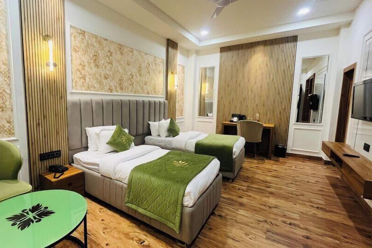 A hotel room with two beds, a green armchair, a small table, a desk, and a TV.