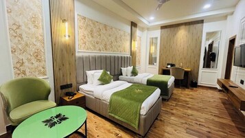 A hotel room with two beds, a green armchair, a small table, a desk, and a TV.