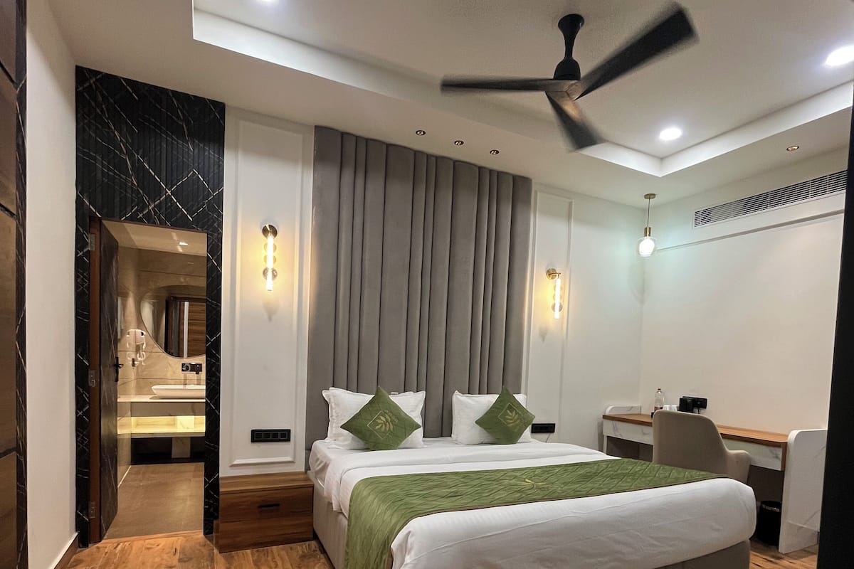 A modern hotel room with a large bed, a desk, and a chair. There is a ceiling fan and recessed lighting.